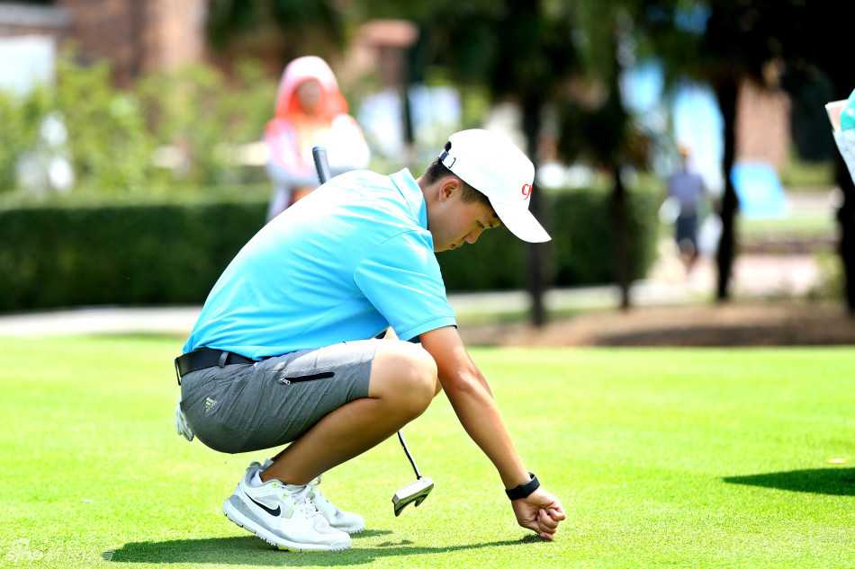 果岭上的友谊之战:海峡两岸高尔夫选手竞技交流纪实 选手屈膝俯身观察果岭,指尖轻触草面,专注神情如同解读大地密码