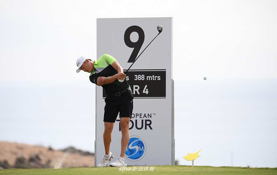 李昊桐与教练在练习果岭边进行交流，手指向果岭方向，似乎在深入探讨推杆线路与力度选择。