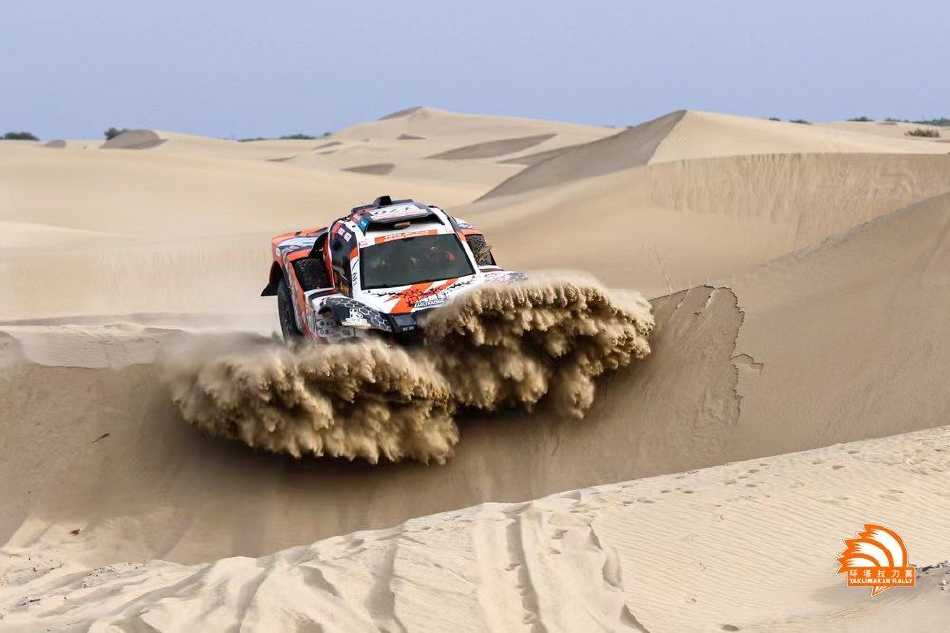 车手专注地操控着方向盘，目视前方崎岖的道路，头盔面罩上倒映着飞速掠过的荒原景象。