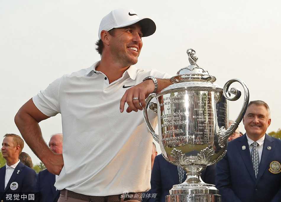 科普卡高举象征PGA锦标赛最高荣耀的沃纳梅克杯，身后是欢呼的观众与绚烂的夕阳。