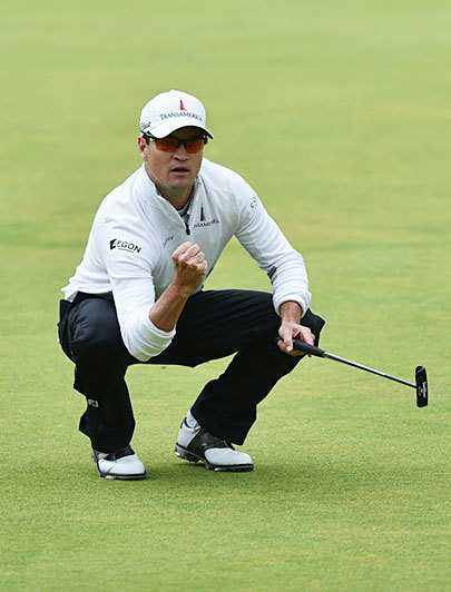 扎克·约翰逊在圣安德鲁斯第18洞果岭振臂庆祝，身后古老的石桥与欢呼的观众见证了他捧起葡萄酒壶的荣耀时刻。