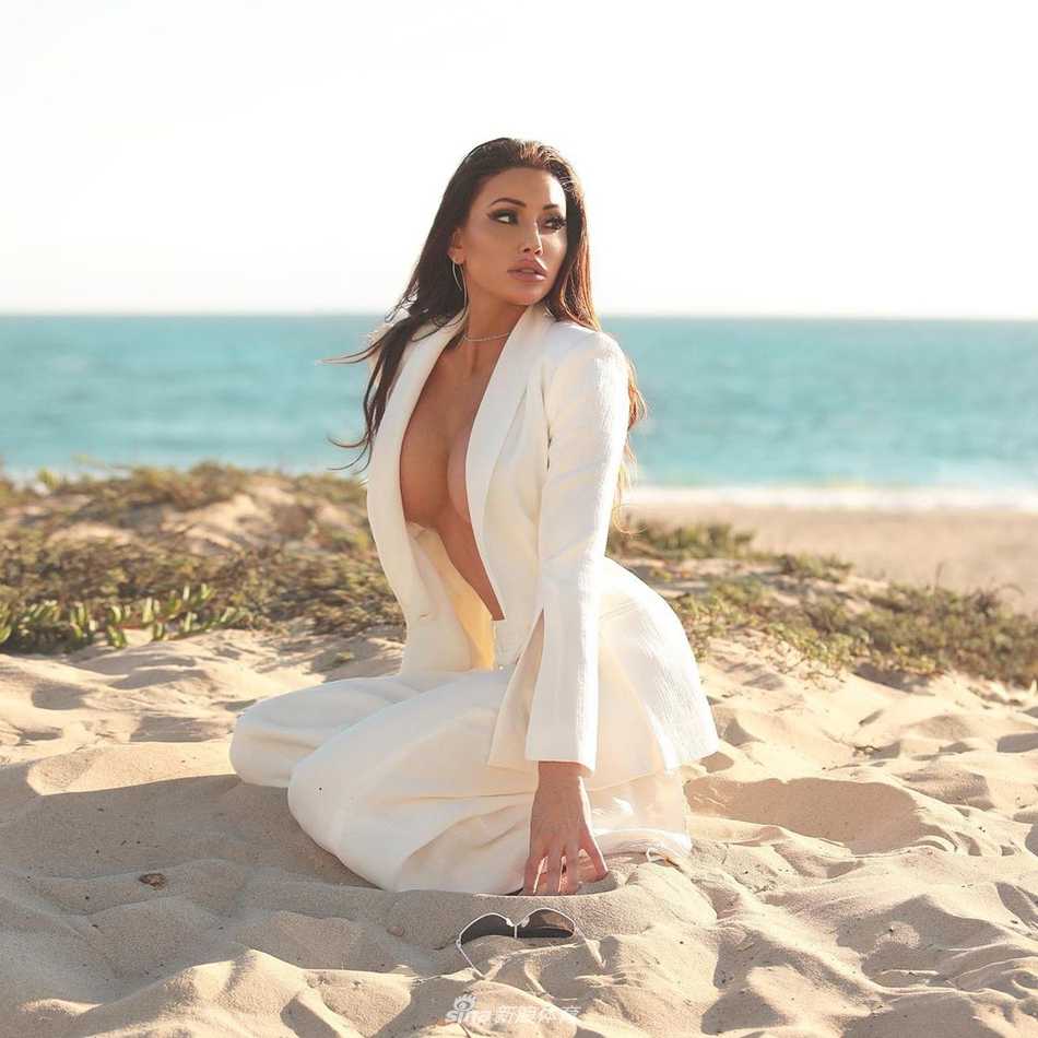 霍莉·桑德斯身穿干练白色西装，手持麦克风，在绿意盎然的球场边进行专业播报，笑容自信而富有感染力。