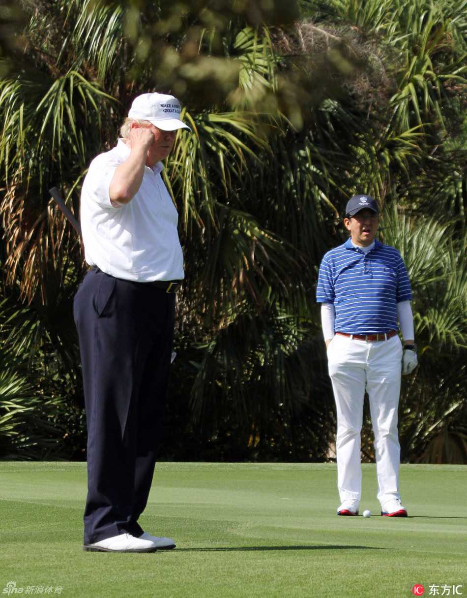 特朗普与安倍晋三在球道上并肩而行，神情轻松地进行交流，背景是开阔的高尔夫球场