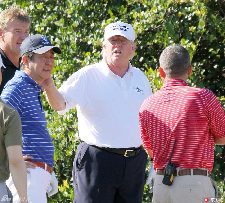 特朗普与安倍晋三并肩站立在开球台上，特朗普手指远方，似乎在讲解球道策略，安倍侧耳倾听
