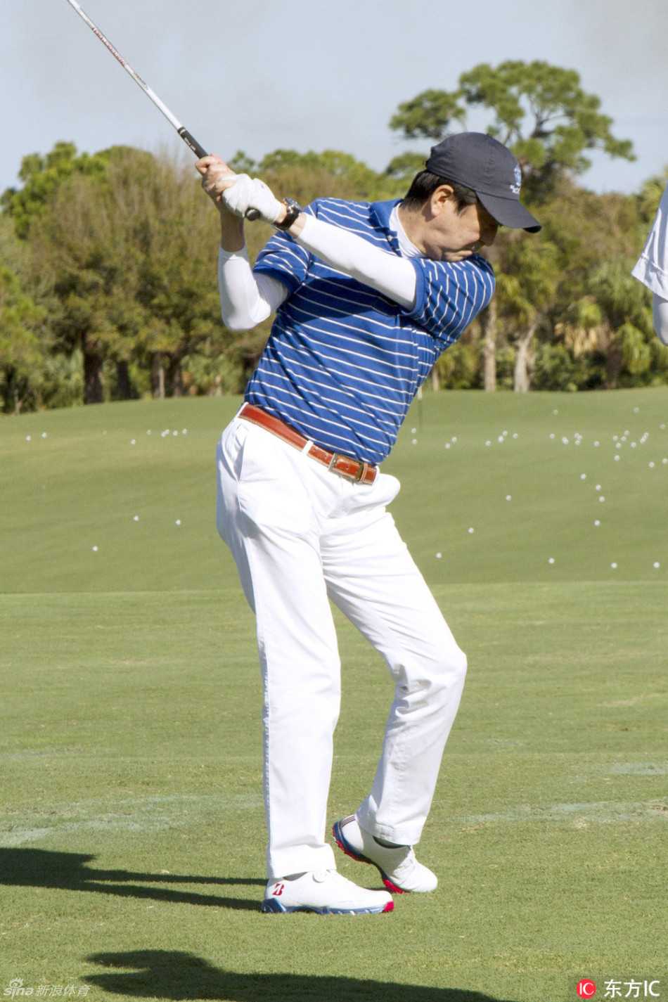 特朗普与安倍晋三面带笑容，高举手臂，在空中击掌庆祝，背景是绿茵果岭