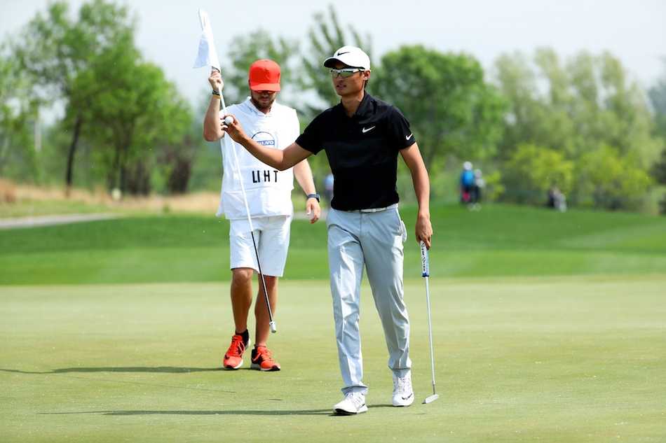 韩国选手文景俊正蹲在果岭边，以极低的视角仔细观察推杆线路的起伏与草纹。