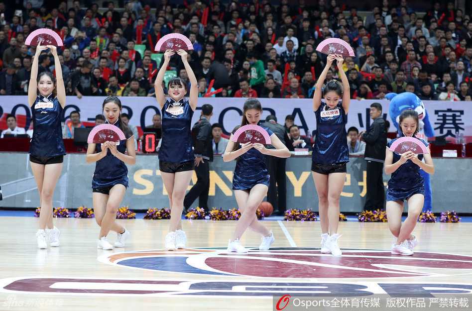 在灯光聚焦的赛场中央，一位篮球宝贝高抬腿展示修长美腿，背景是巨大的CBA联赛标志和热情的观众。