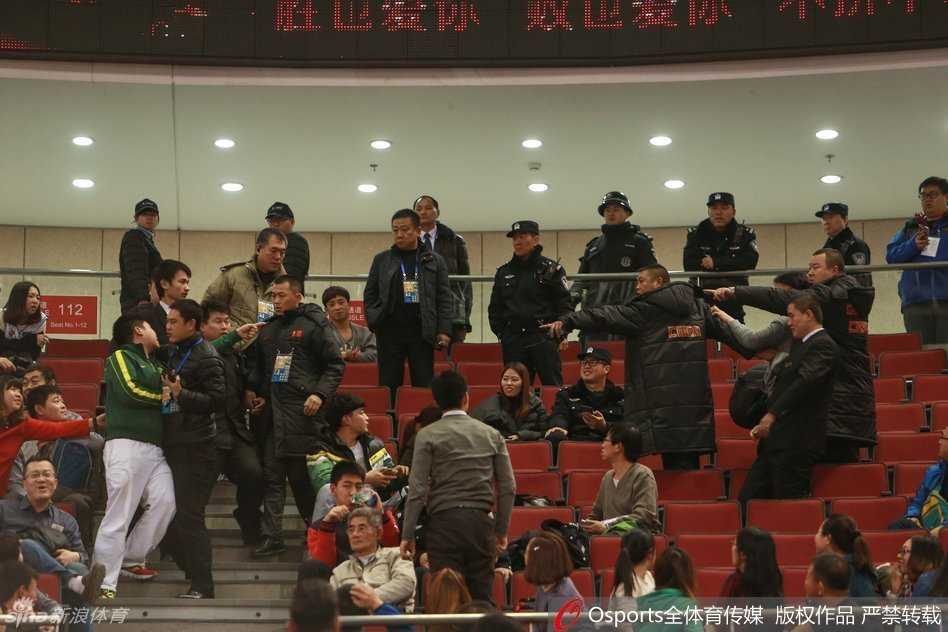 看台上的混乱仍在继续，一名身穿深色外套的球迷被身边多人紧紧拉住，他身体前倾，面部因情绪激动而扭曲，似乎试图冲向某个方向。周围原本坐着的观众纷纷站起，目光全部聚焦于这处骚动的中心，赛场内的秩序管理面临严峻考验。