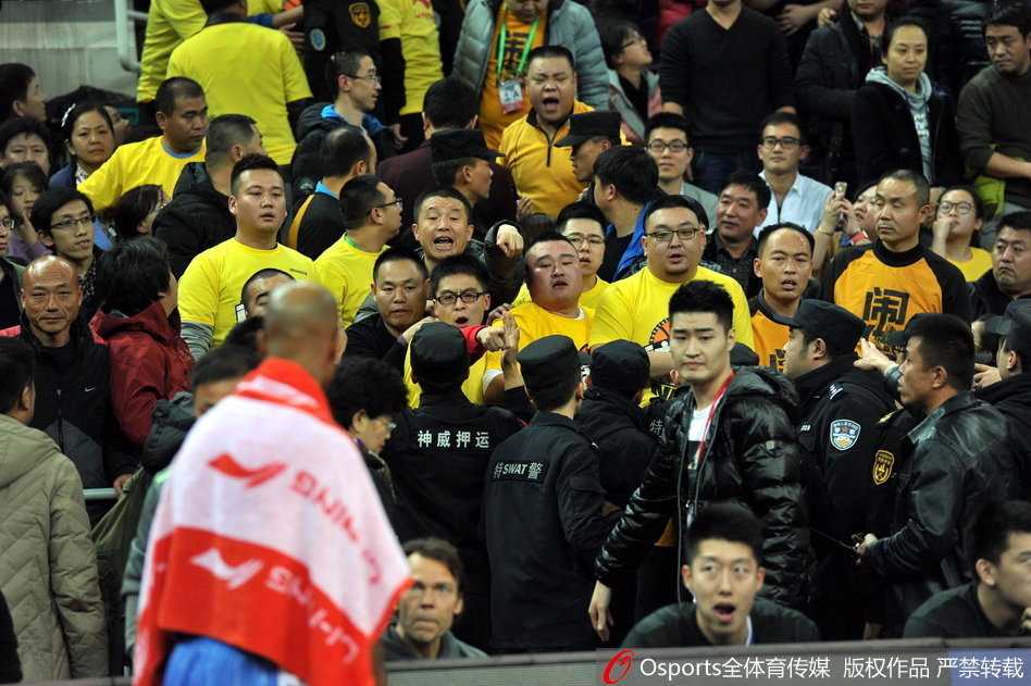 混乱之中，一名身着深色外套的球迷试图冲破安保人员的阻拦，他的身体前倾，手臂用力地向前伸，而在他面前，一名年轻的安保人员正全力阻挡，表情坚毅而吃力。