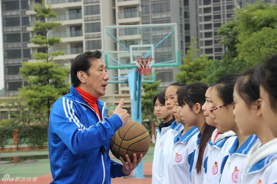 李群弯腰俯身纠正小队员的运球姿势，眼神专注，手把手教学