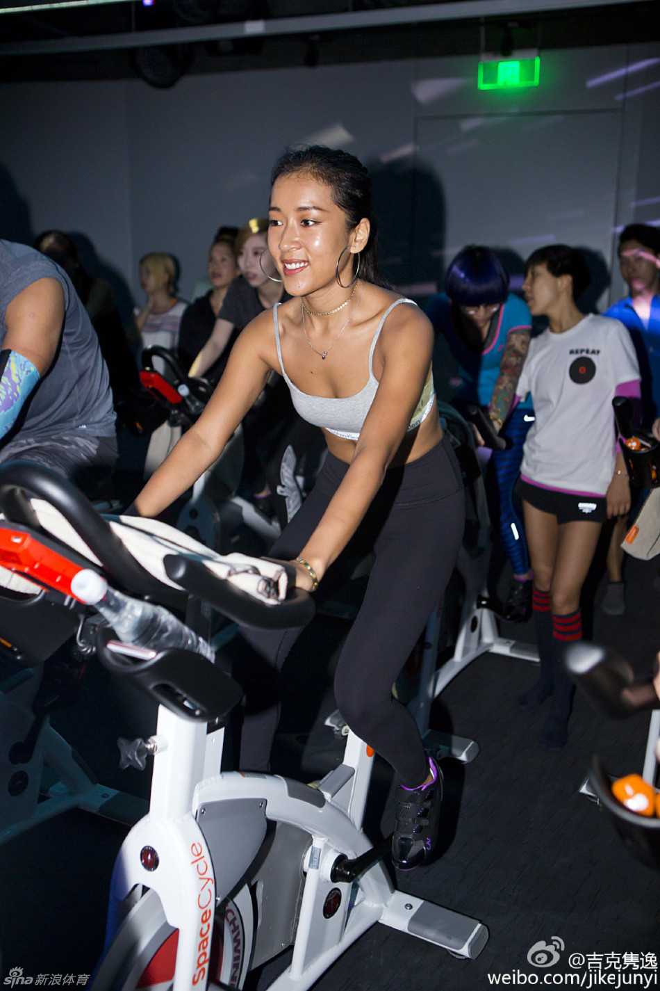 吉克隽逸与中国男篮队员们合影，她被高大的球员们簇拥在中间，脸上带着灿烂又有些俏皮的笑容，一身红色队服格外醒目，画面充满动感与和谐