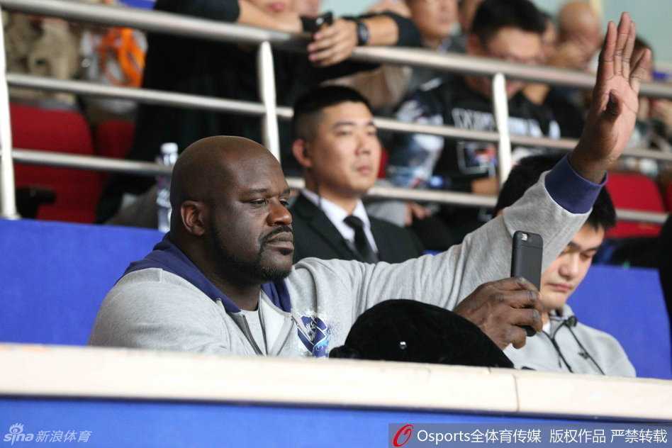 奥尼尔调皮地拿起手机对准姚明拍照，而姚明则面带微笑地看向镜头，两人之间的互动充满了老友重逢的趣味与温馨。