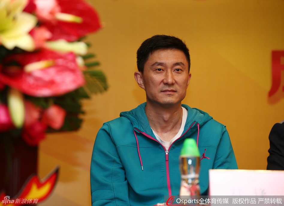 宏远酒店宴会厅内，杜锋身着深色西装，双手插袋侧身倾听，眼神专注地投向发言席，背景板上的公司名称格外醒目，现场气氛庄重而热烈。