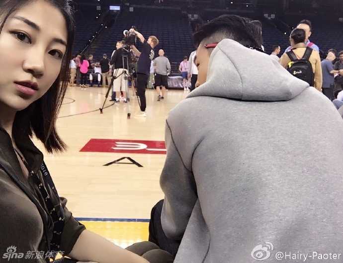 训练间隙，李跑来到场边的记者工作区，以球场为背景俏皮自拍。远处，一群手持长枪短炮的摄影记者正严阵以待，他们的镜头统一对准了场内正在进行投篮热身的球员，形成了一道独特的赛场风景线。