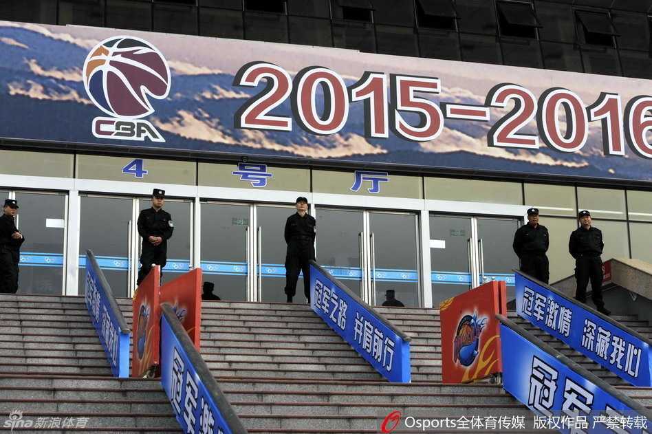 银色水炮车在体育馆外严阵以待，庞大的身躯和高压水枪在阳光下泛着冷光，仿佛沉默的钢铁巨兽，随时准备应对任何突发骚乱。