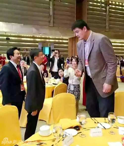 姚明与马云同桌就座，两人相邻而笑，虽然身高差依然明显，但笑容同样灿烂。