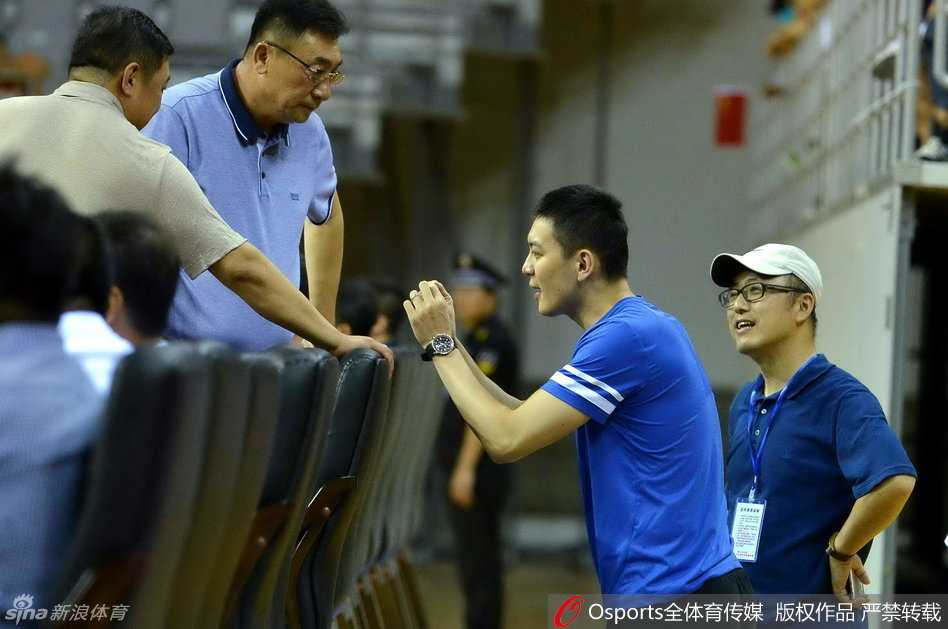 杨鸣在场边看得入神，身体微微前倾，双手交叉，全神贯注于比赛进程，身边放着那瓶陪伴他观赛的水。