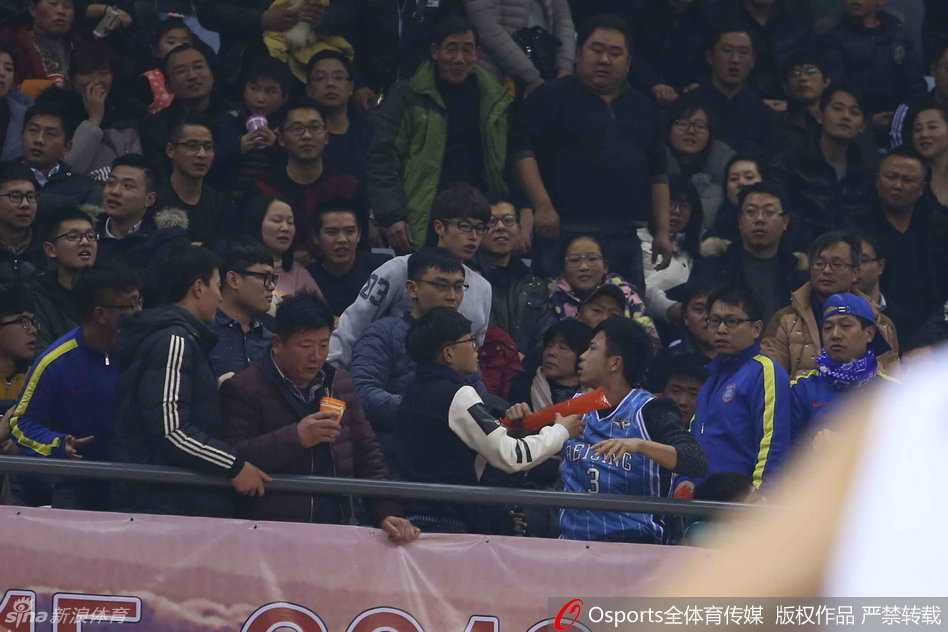 冲突区域周围的球迷纷纷站立，目光聚焦在扭打的人群上，很多人面露愤怒和不满，有人指着冲突方向大声斥责