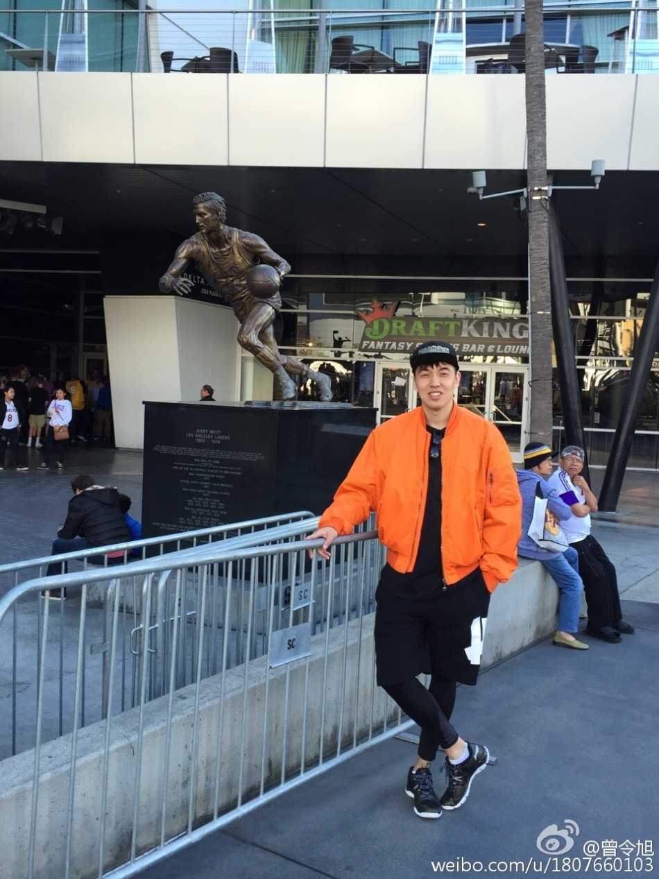 斯台普斯中心内场，曾令旭身穿醒目的科比24号球衣，举起手中的科比摇头娃娃，身后是即将见证历史的狂热球迷海洋