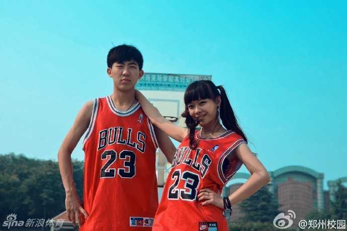 校园篮球比赛夺冠后，在众人的欢呼和蓝色的篮球场地板上，男孩激动地拥抱着女孩深情亲吻，女孩也紧紧搂着男孩的脖子，画面充满了胜利的喜悦和恋爱的甜蜜。