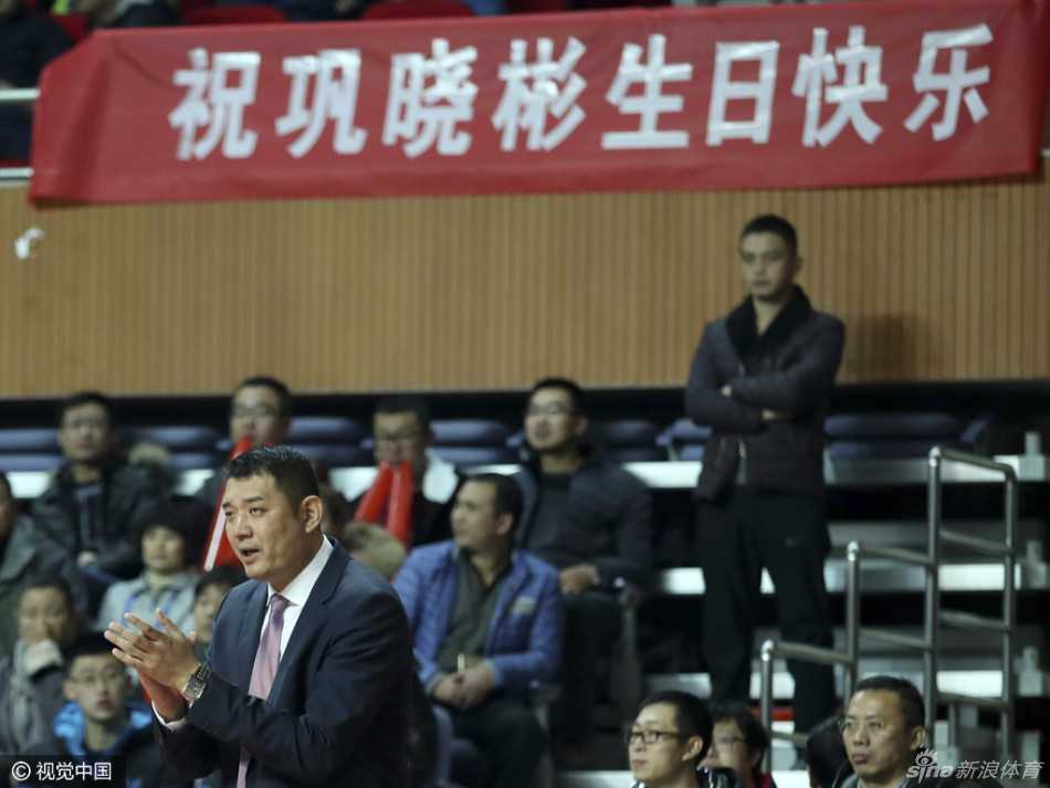 巩晓彬在赛后面带微笑地向球迷致意，他身边围绕着多名青岛队的球员，大家虽然没有赢球，但依然手拿球迷赠送的礼物，共同感受着来自支持者的温暖，背景是潍坊学院体育馆的通道。