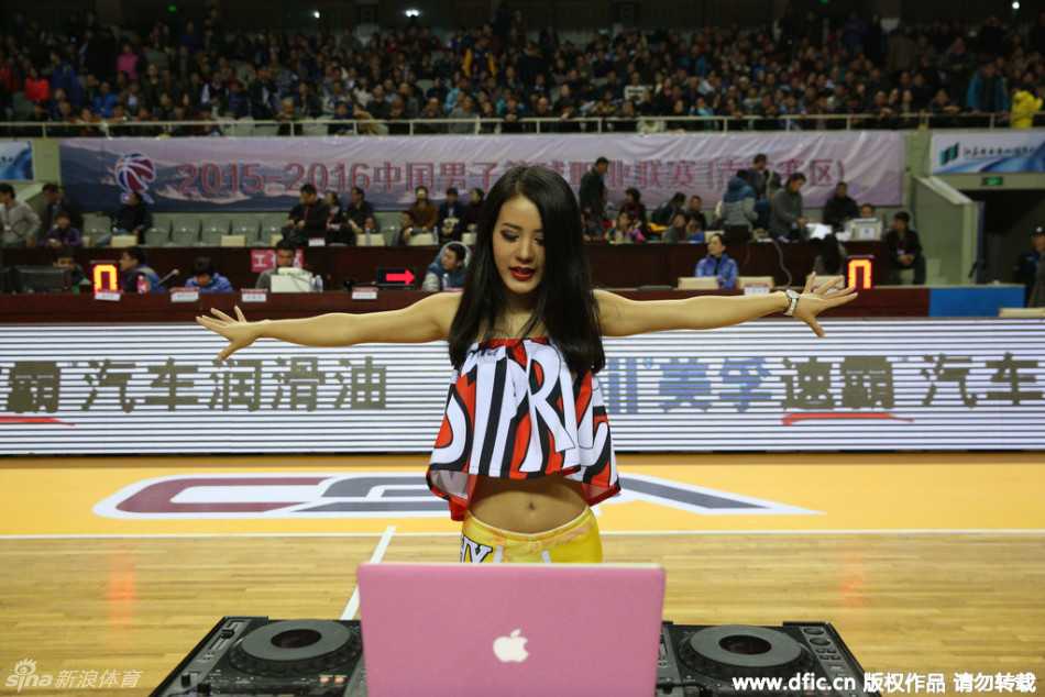 她安静地坐在DJ台前，手指轻触调音设备，双眸闪烁着温柔光芒，与身后热闹的赛场形成一幅动人的画面