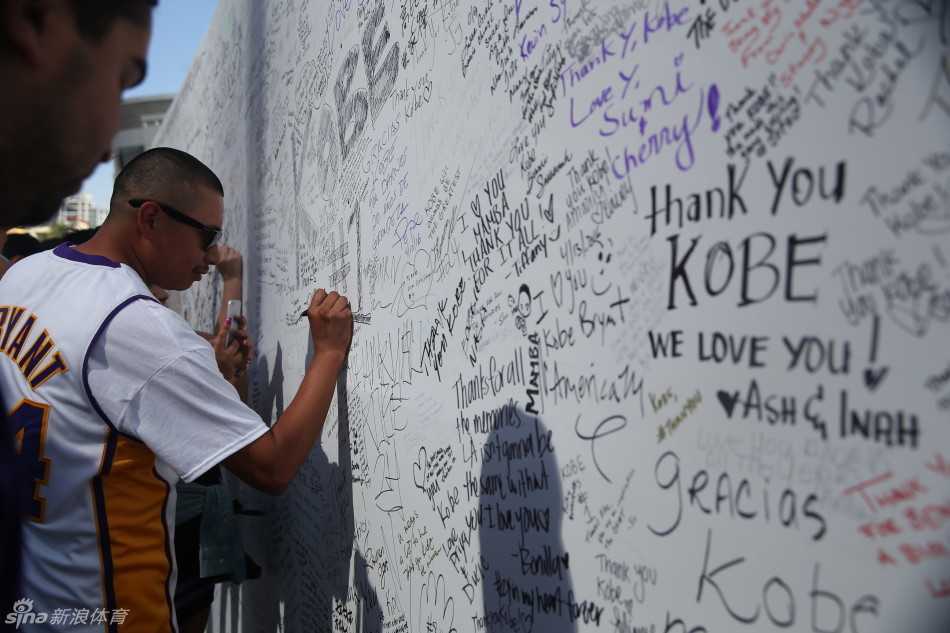 斯台普斯中心外，一位眼神清澈的小球迷穿着过大的科比球衣，手持加油标语，在父母的陪伴下静静等待偶像的最后一舞。