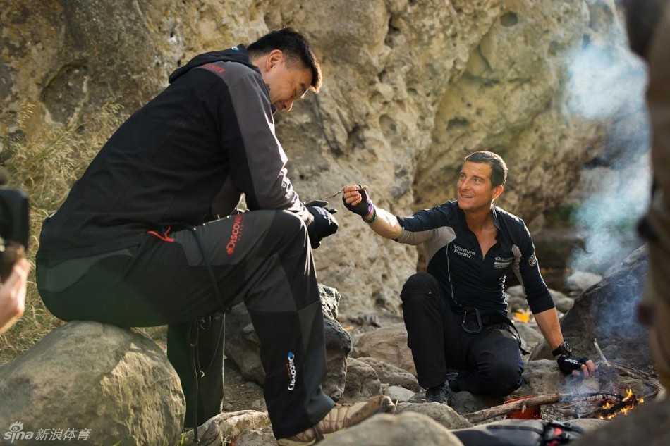 荒野之上，贝爷手持“高蛋白零食”递向姚明，眼神中满是期待；而姚明则眉头微蹙，嘴角扬起一抹标志性的姚氏苦笑，仿佛在问：兄弟，能不能换块牛排？