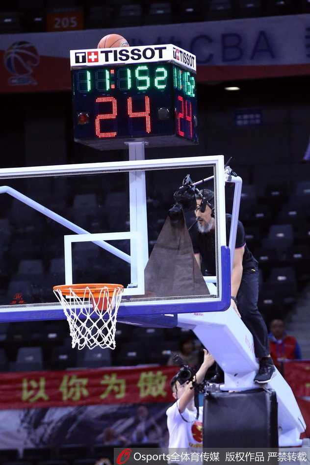 一名勇敢的工作人员爬上高高的篮球架，正伸出手臂去取卡在计时器上的篮球