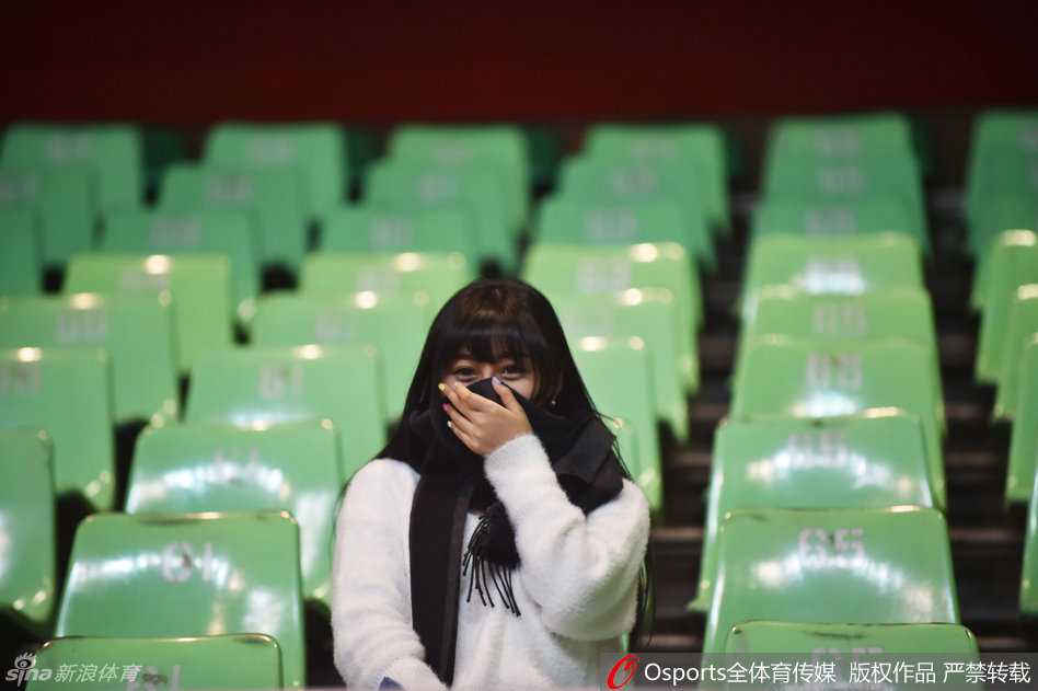 一位戴着眼镜的知性美女球迷在场边回眸，手中拿着门票，温婉的气质与火热的赛场形成美妙的对比