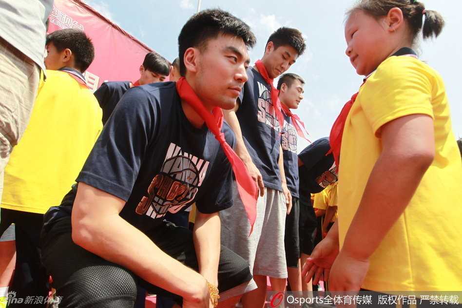 辽篮岫岩公益行 李晓旭与孩子们共筑篮球梦 在校园操场上,辽篮队员李晓旭正与一群小学生进行篮球互动,他耐心地指导着孩子们的基础动作,画面温馨。