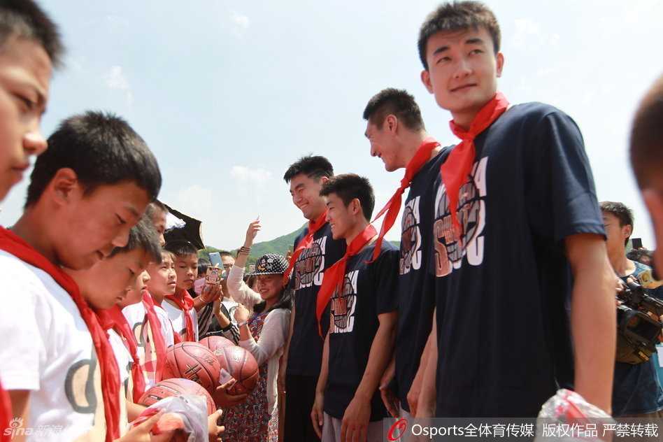 辽篮岫岩公益行 李晓旭与孩子们共筑篮球梦 辽宁飞豹男篮全体将士与李大堡小学的师生们站在一起,在校园教学楼前拍摄大合影,所有人都面带笑容,气氛融洽。