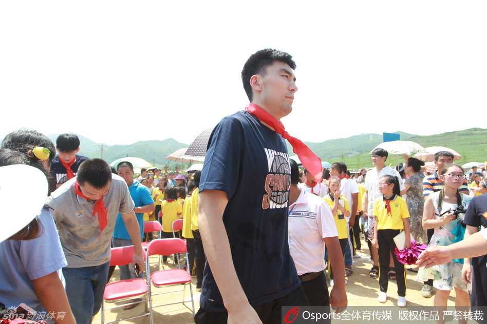 辽篮岫岩公益行 李晓旭与孩子们共筑篮球梦 一名少先队员正在为李晓旭佩戴红领巾,李晓旭微微低头配合,脸上洋溢着温暖的笑容,旁边站满了鼓掌的师生。