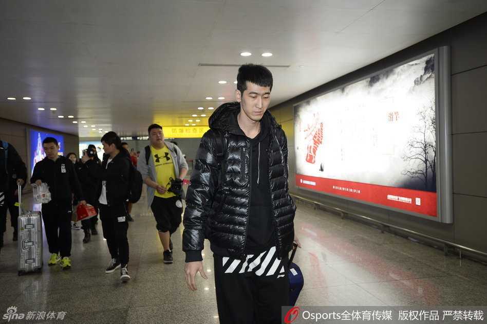 走出机场通道的郭艾伦面对镜头，尽管表情略显疲惫，但眼神中透露出一股不服输的倔强，身后是紧紧跟随的安保和涌动的人潮。