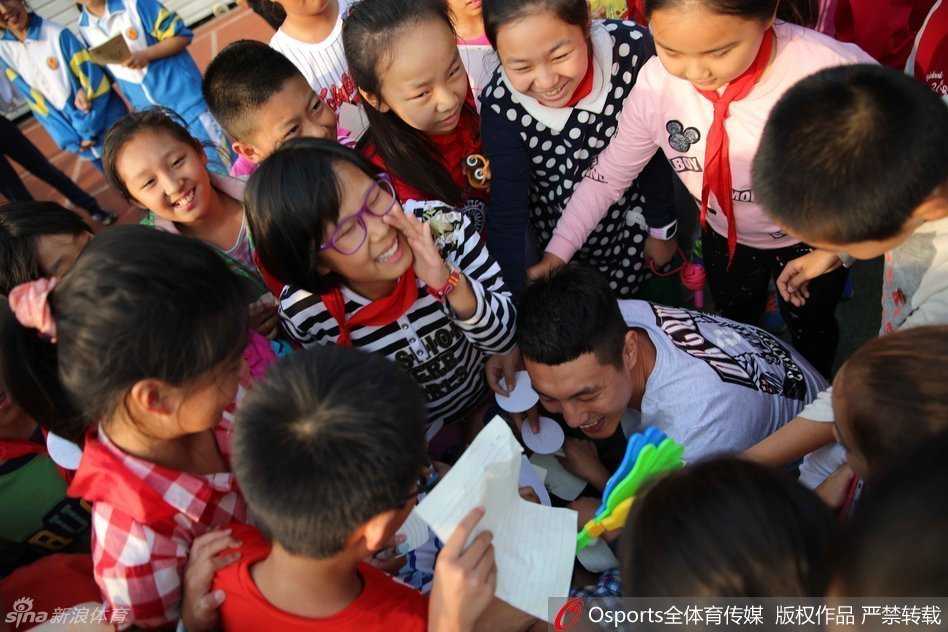 吉喆和翟晓川正在为小朋友们做投篮示范，两人高大的身影与孩子们形成鲜明对比，吉喆认真指导动作，孩子们目不转睛地学习