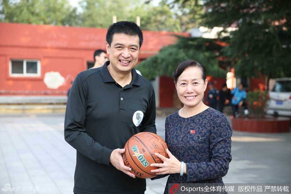 主教练闵鹿蕾现身活动现场，正弯着腰给一位小朋友讲解篮球战术，神态专注而慈祥，孩子们围在一旁认真听讲