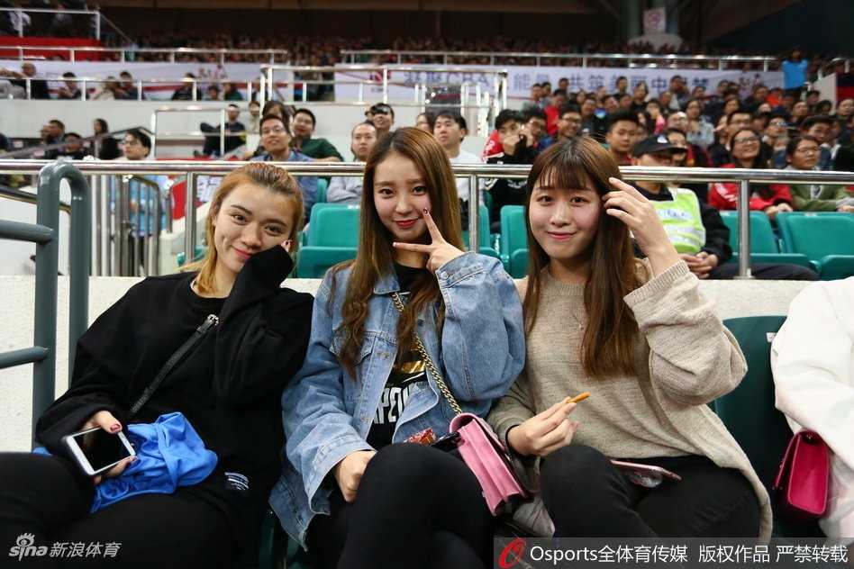 一位气质清冷的美女球迷坐在场边，她专注的目光越过喧嚣的人群，紧紧锁定在激烈的赛场之上，仿佛周遭的一切都无法打扰她对篮球的纯粹热爱。