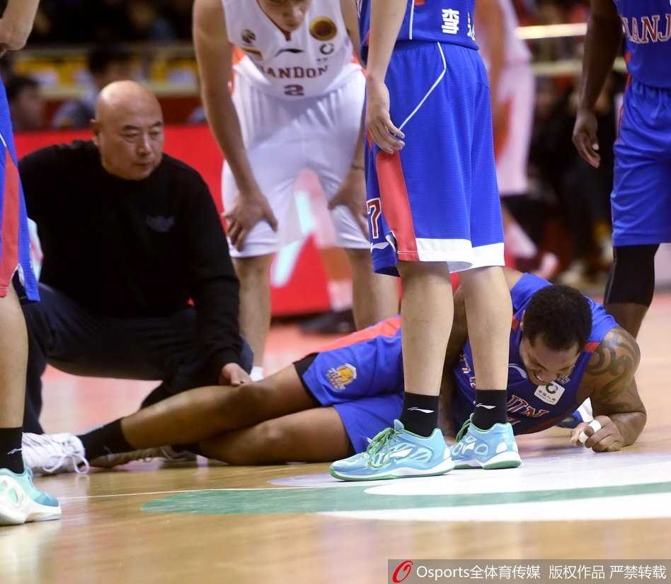 CBA赛场惊魂一刻:天津队外援霍尔曼髌骨脱位重伤离场 救护人员用担架将沉重的霍尔曼抬起,场边的广告牌和观众席虚化成背景,几名天津队队员默默跟在担架旁护送,目送他们的内线核心离场。