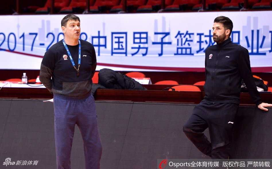 主教练凯撒在场边双手比划着战术，丁彦雨航双手叉腰认真聆听，身旁的莫泰尤纳斯也侧身关注，教练组的战术布置详尽而具体。