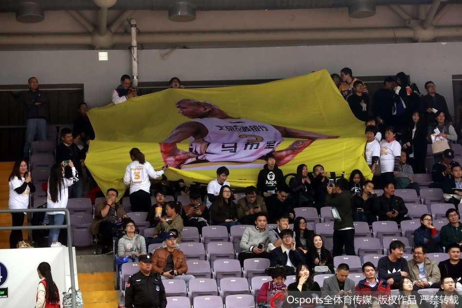 比赛进入白热化阶段，马布里在弧顶持球观察队友跑位，身后的看台上，他那幅巨大的黑白肖像海报如同守护神一般俯瞰着全场，与看台上涌动的人潮构成了一幅令人动容的画卷。