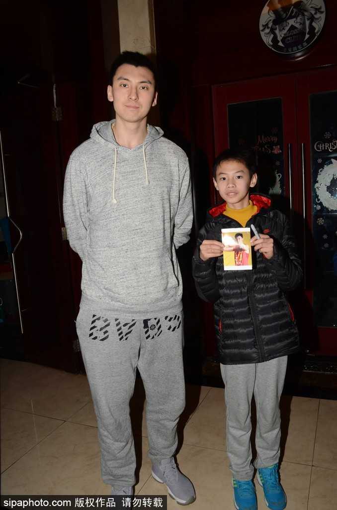 方硕戴着黑色棒球帽，专注地为球迷在球衣上签名，背景里满是期待的目光和手机镜头