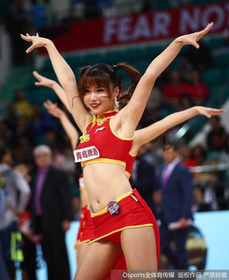 一位宝贝在队伍前列做出俏皮可爱的眨眼动作，双手轻点在脸颊旁，仿佛在向看台上的球迷发送一颗甜蜜的爱心，瞬间融化了无数镜头。