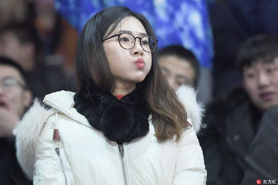 一位身着粉色宽松卫衣的俏皮女生，扎着清爽马尾，在吉林主场震天的助威声中，露出惊喜又羞涩的笑容，仿佛被镜头捕捉到了小心思