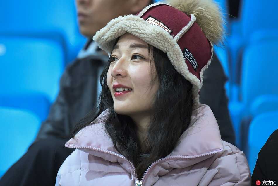 一位戴着时尚毛线帽的女生侧身回眸，长长的睫毛和精致的侧颜在体育馆的灯光下显得格外动人，身后是模糊的座位和人海，宛如电影画面