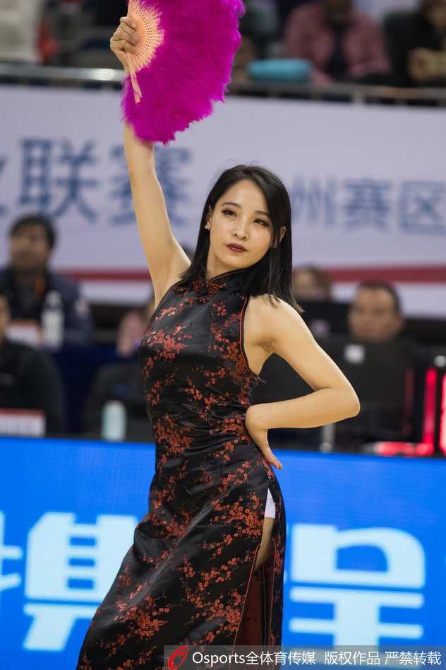 在体育馆的背景映衬下，一位啦啦队员轻抚秀发，眉眼含笑，旗袍的温婉与身后巨大的CBA标识形成有趣的视觉对比。