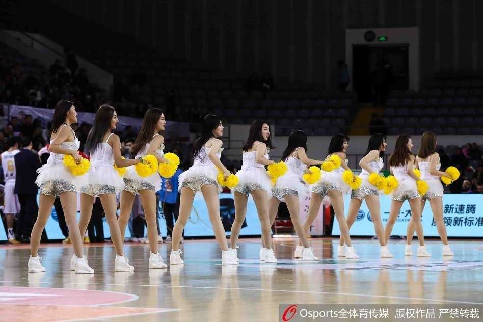 北控篮球宝贝们身穿着红白相间的活力装束，在赛场中央整齐列队，她们高抬手臂，脸上洋溢着灿烂的笑容，仿佛冬日里的暖阳一般耀眼夺目。