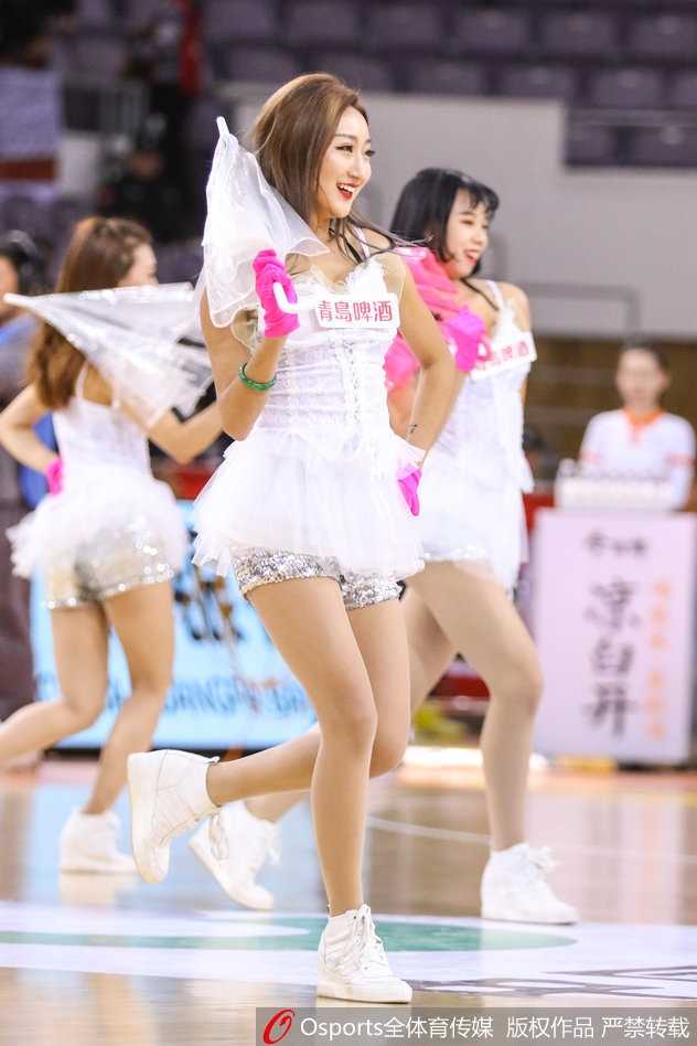 一名篮球宝贝的特写镜头，她微侧着头，眼神中带着一丝俏皮与妩媚，精致的妆容在球场灯光下显得格外动人，展现了新生代啦啦队员的青春风采。