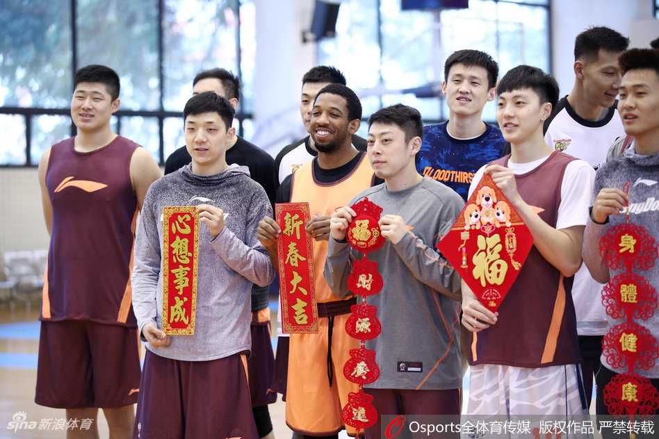 宏远队员们并排站立，手中举着春联和福字，彼此间眼神交流默契十足，画面充满了大家庭团聚般的温馨与和谐气氛。