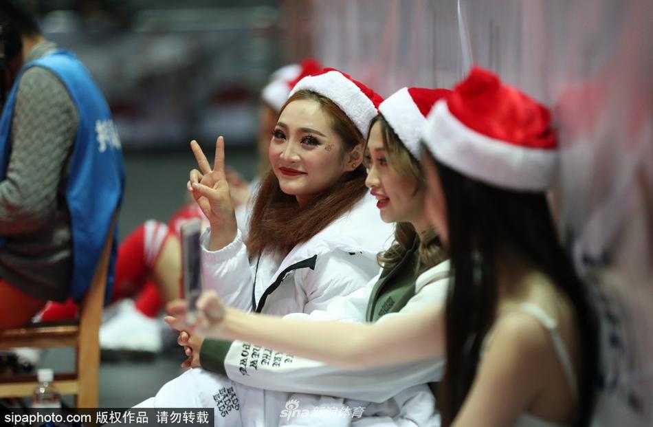 一位宝贝正在对镜整理妆容，旁边的队友拿着手机充当光线的补充板，即使在嘈杂的球场角落，她们也要保持最完美的形象面对观众。