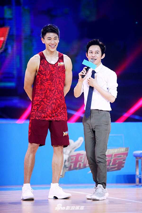 奥尼尔张开双臂试图阻拦开着移动篮筐小车的宋茜，巨大的体型差形成鲜明对比，场面欢乐如同大人与孩子的嬉戏